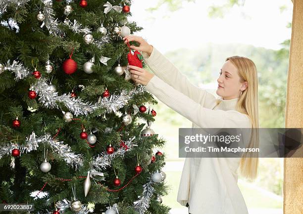 teenage girl hanging decorations on christmas tree - halstock stock-fotos und bilder