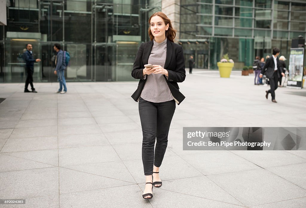 Woman walking in city holding smartphone