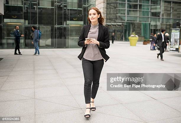 woman walking in city holding smartphone - woman walking full length stock pictures, royalty-free photos & images