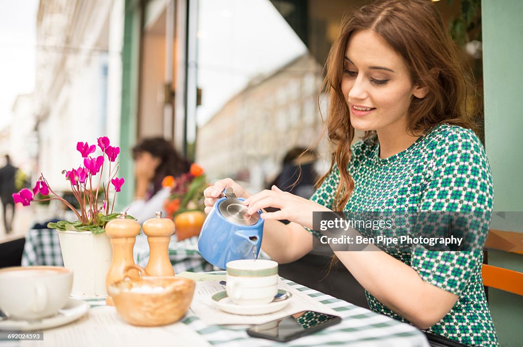 Woman at pavement cafe pouring from teapot