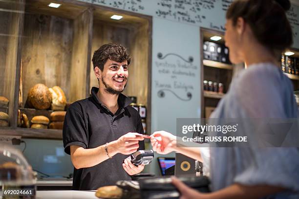 barista handing credit card to female customer at cafe counter - man offering bread stock pictures, royalty-free photos & images