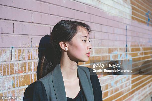 portrait of young woman leaning against graffiti brick wall - graffiti on brick wall stock-fotos und bilder