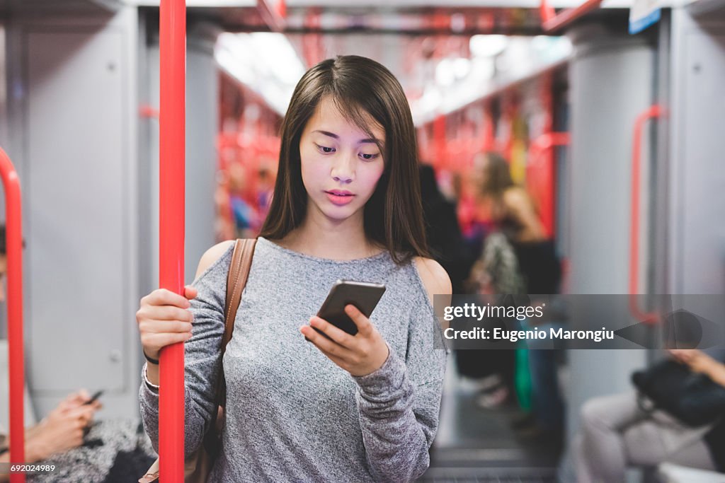 Young woman traveling on train carriage reading smartphone texts