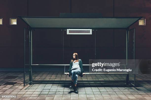 young woman sitting at bus stop at night - bushaltestelle stock-fotos und bilder