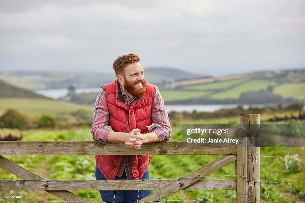 Man on farm leaning against gate looking away