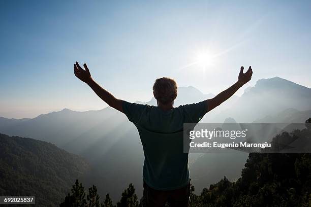 rear view of man, arms raised looking at view of mountains, passo maniva, italy - arms outstretched mountain stock pictures, royalty-free photos & images