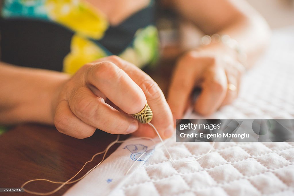 Cropped view of woman sewing hem on quilt