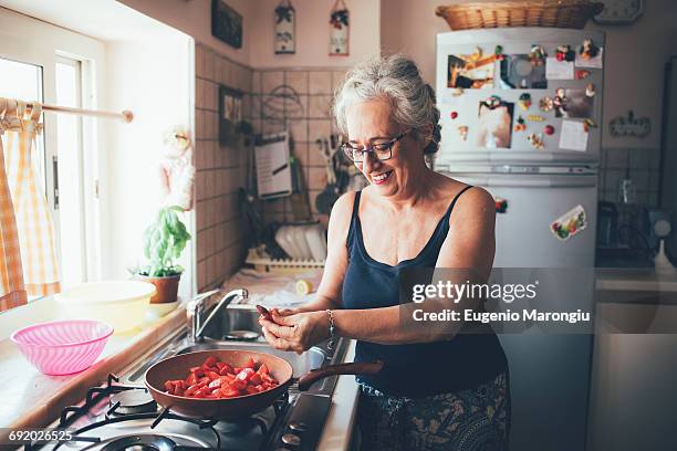 woman chopping tomatoes into saucepan smiling - middle aged woman at home stock pictures, royalty-free photos & images