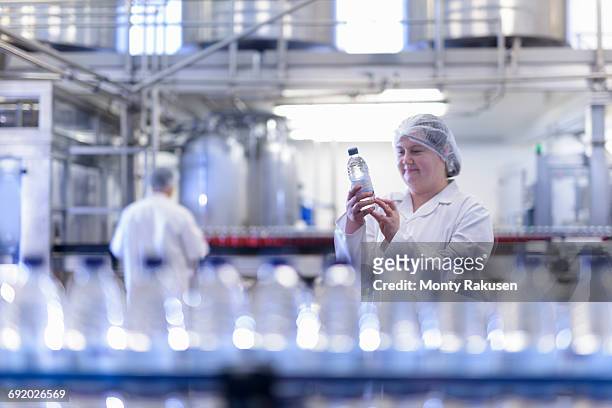 female worker inspecting water bottle on production line in spring water factory - bottle factory stockfoto's en -beelden