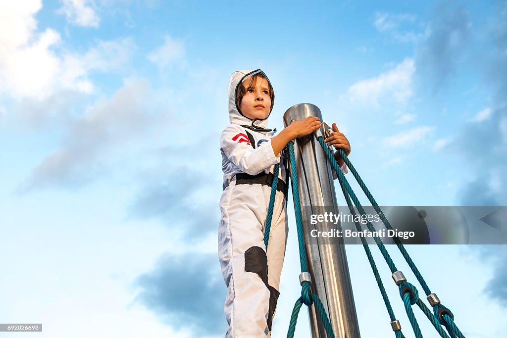 Boy in astronaut costume looking out from top of climbing frame