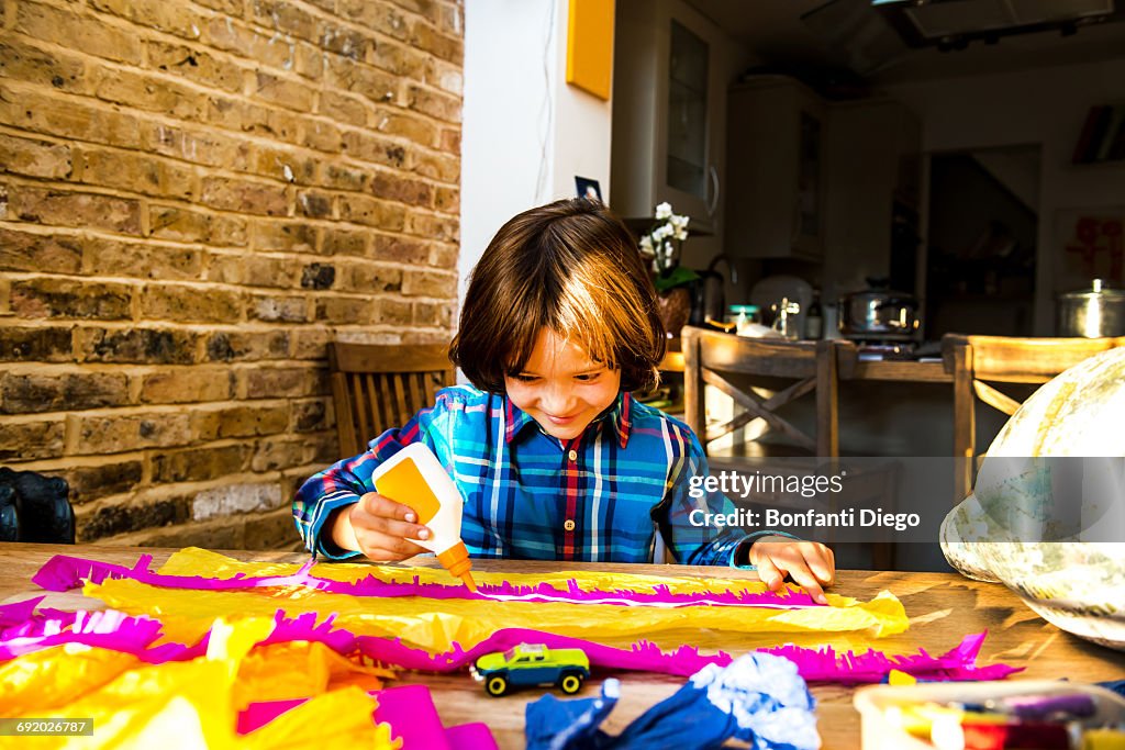 Boy spreading glue on crepe paper to make pinata