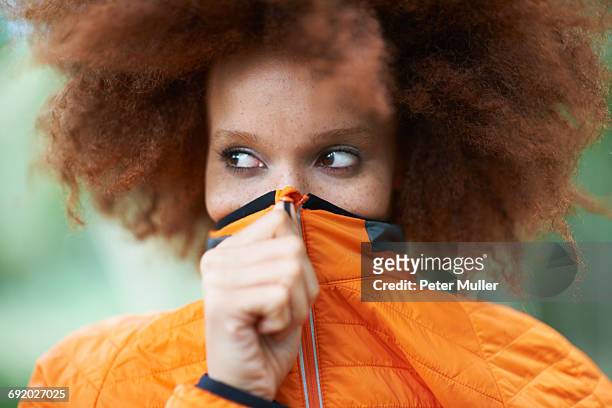 portrait of woman covering mouth with coat looking away - mão na boca imagens e fotografias de stock