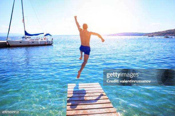 uomo allegro che salta in acqua - jumping of boat foto e immagini stock