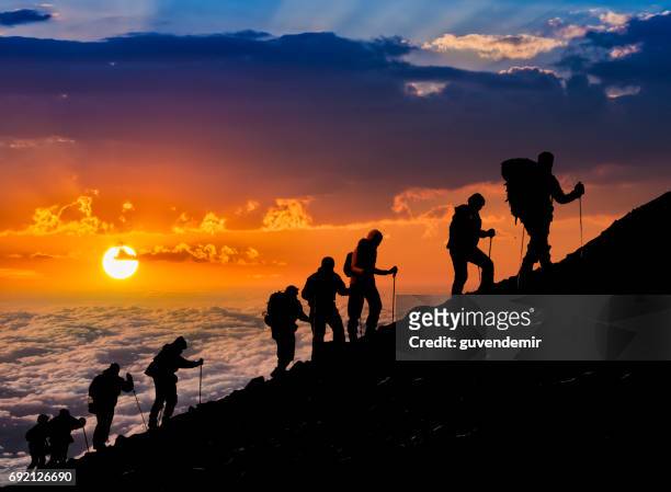 silhouettes of hikers at sunset - people climbing walking mountain group stock pictures, royalty-free photos & images