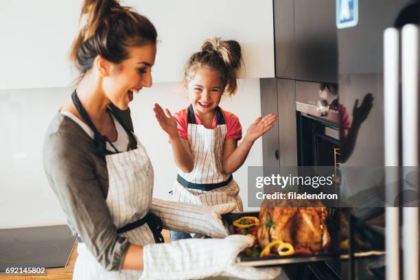 mother taking the dinner out of the oven - mother and child cooking stock pictures, royalty-free photos & images