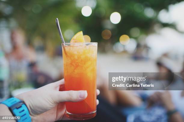 hand holding bright red and orange frozen cocktail on the beach - frozen drink stock pictures, royalty-free photos & images