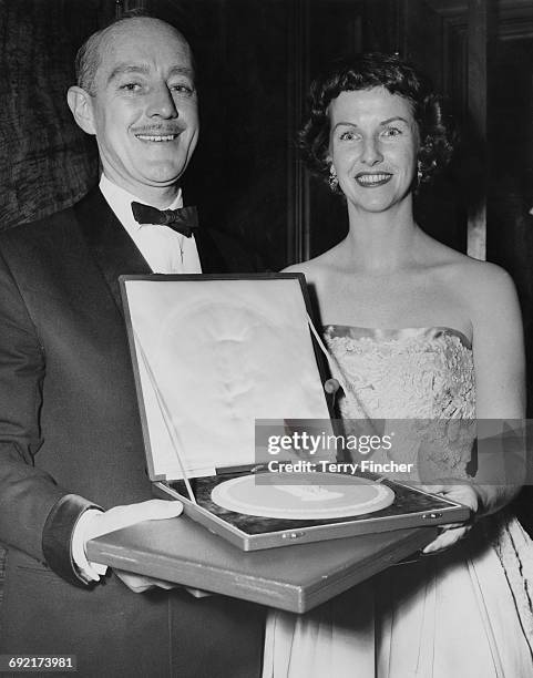 English actor Alec Guinness holding the award he has accepted on behalf of actress Katie Johnson for her role in 'The Ladykillers', at the British...