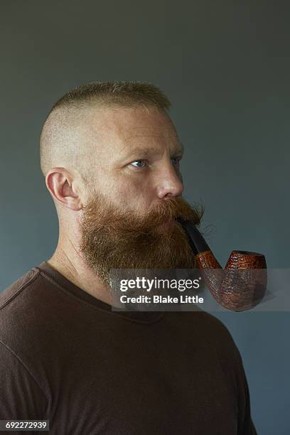 bearded pipe smoking man studio portrait - corte de pelo con media cabeza rapada fotografías e imágenes de stock