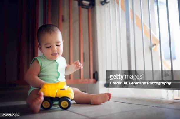 11 month old plays with a yellow toy truck in the house - baby gate stock pictures, royalty-free photos & images
