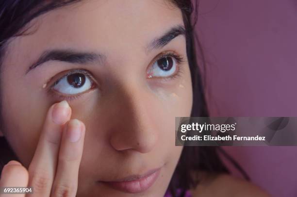 young woman blending concealer under her eyes. - compassionate eye fotografías e imágenes de stock