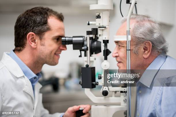 senior patient getting an eye exam at the optician - eye test equipment imagens e fotografias de stock