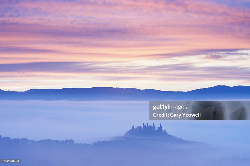 Farmhouse in misty Tuscan landscape at dawn