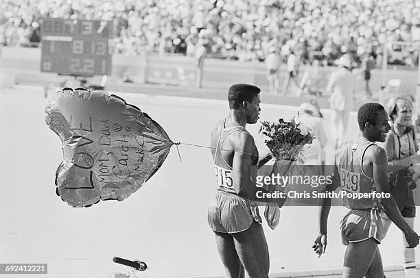 American athlete and sprinter Carl Lewis celebrates with a bouquet of flowers and a large balloon with text 'Love from mom, dad, Carol, Mack & Cleve'...