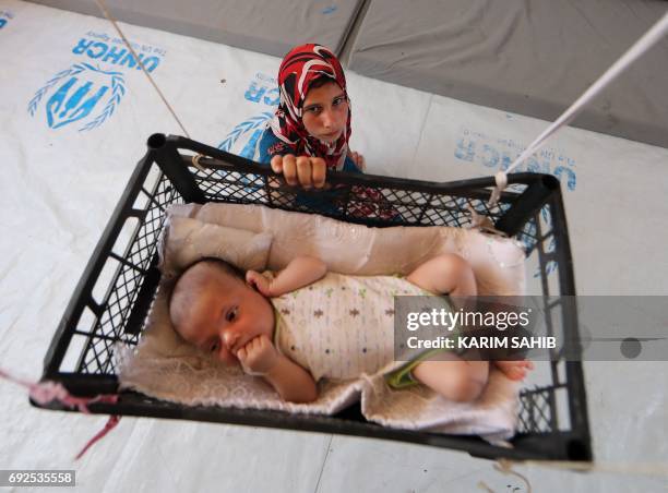 Picture taken on June 5, 2017 shows a displaced Iraqi girl swinging her brother, who is sleeping in a makeshift crib made from a fruit-basket as it...