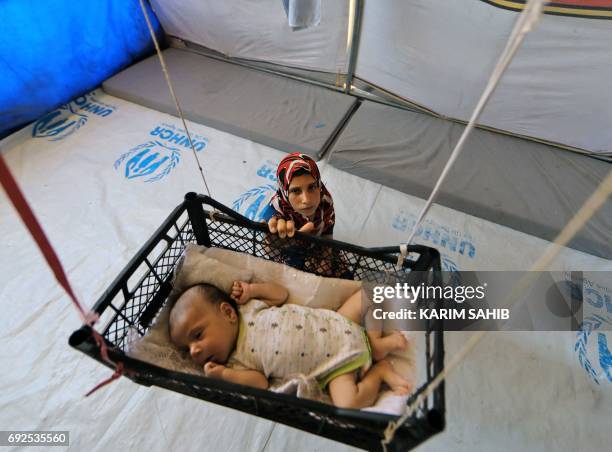 Picture taken on June 5, 2017 shows a displaced Iraqi girl swinging her brother, who is sleeping in a makeshift crib made from a fruit-basket as it...