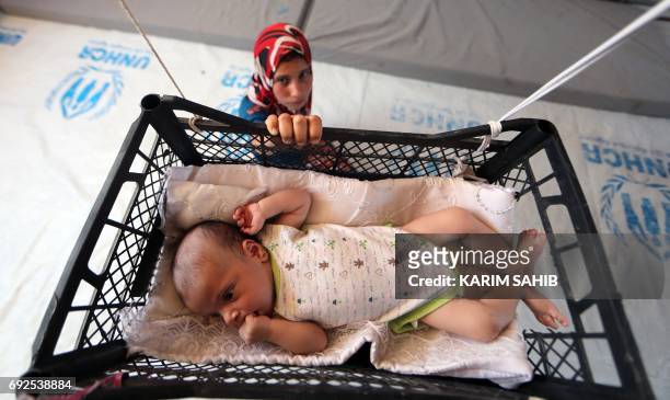 Picture taken on June 5, 2017 shows a displaced Iraqi girl swinging her brother, who is sleeping in a makeshift crib made from a fruit-basket as it...