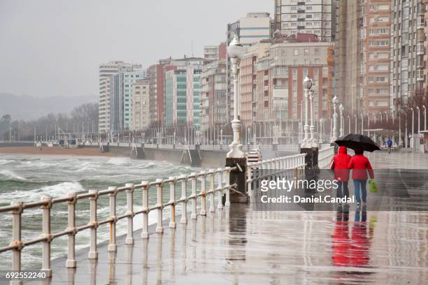 two people walking in gijon promenade during stormy day. gijón, asturias (spain) - chuva imagens e fotografias de stock