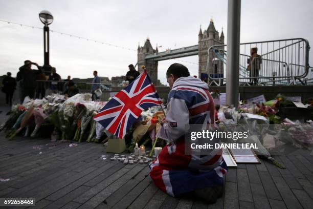 Man holds a Union flag as he kneels near flowers layed at Potters Fields Park in London on June 5 during a vigil to commemorate the victims of the...