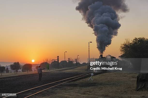 a railway signal man at sunrise giving a green flag to a locomotive passenger train to begin its journey. pretoria, gauteng province, south africa - locomotive fotografías e imágenes de stock