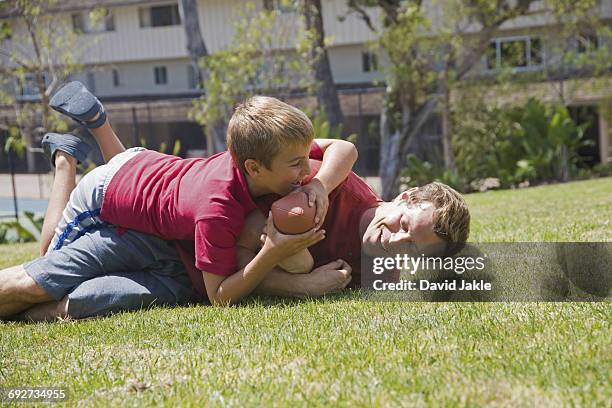 boy tackling father playing american football in park - rough housing stockfoto's en -beelden