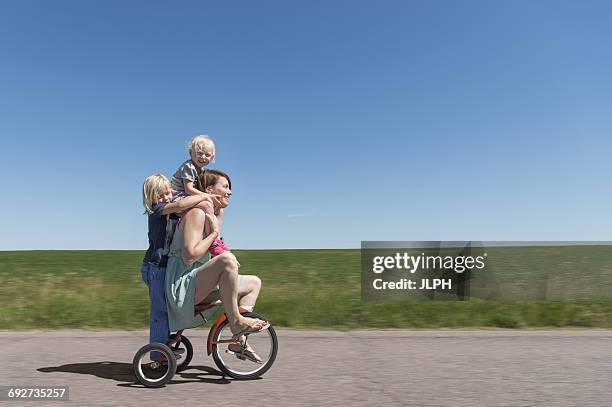 side view of mother and children riding tricycle in rural area - crazy youngster stock pictures, royalty-free photos & images