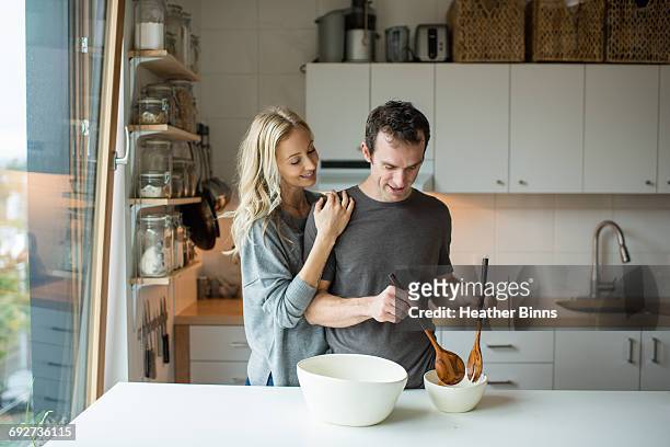 mid adult couple mixing salad bowl in kitchen - rolwisseling stockfoto's en -beelden