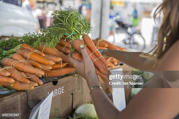 woman at fruit and vegetable stall selecting carrots - venice californie photos et images de collection