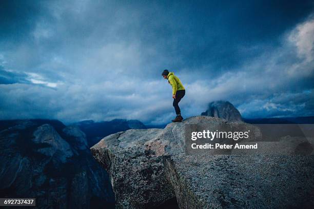 mid adult man standing at top of mountain peering over edge, yosemite national park, california, usa - über etwas schauen stock-fotos und bilder