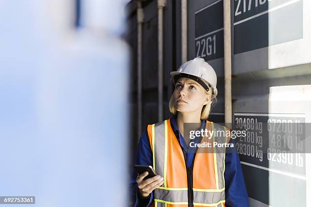 female worker holding mobile phone in shipyard - dock worker stock-fotos und bilder