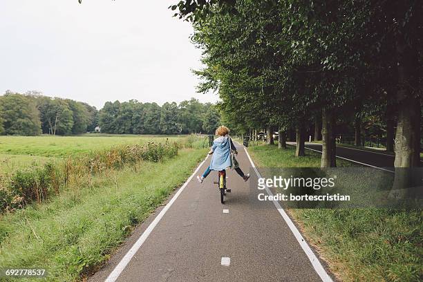 rear view of woman riding bicycle on road - olanda settentrionale foto e immagini stock