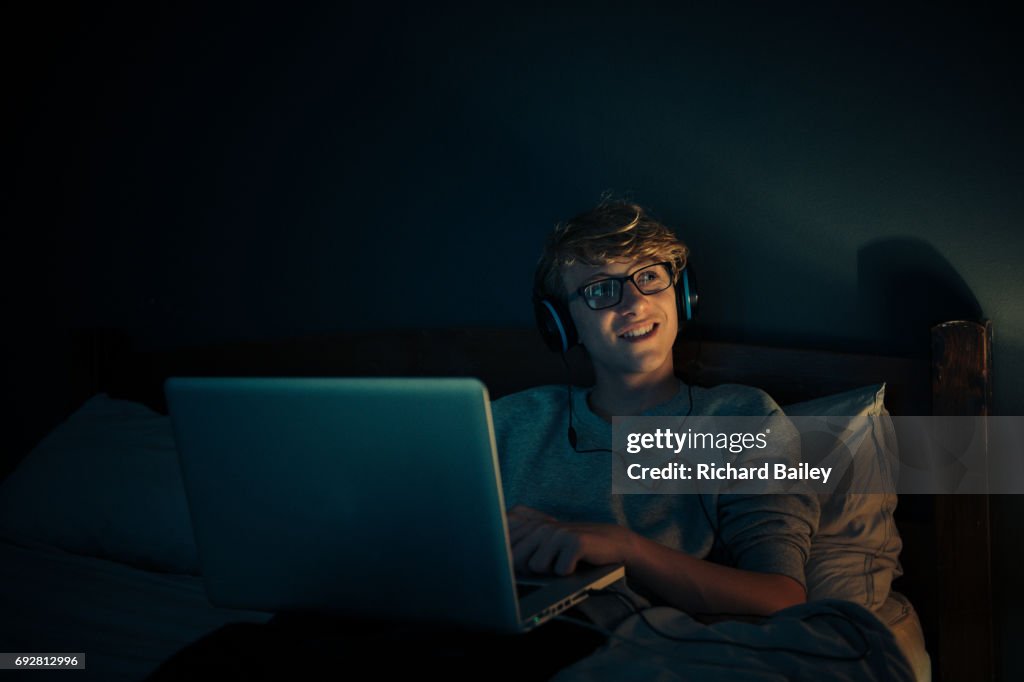 Teenage boy looking at computer in bedroom at night