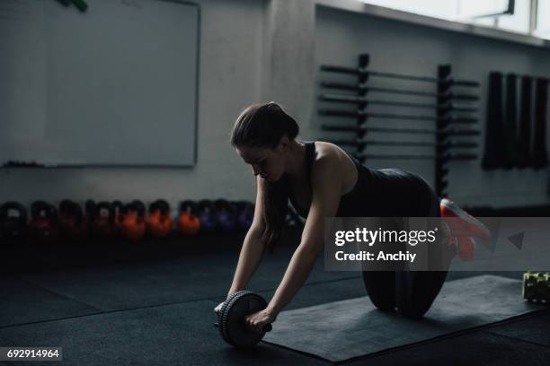 young woman training with wheel to strengthen her abdominal muscle - training wheels stock pictures, royalty-free photos & images