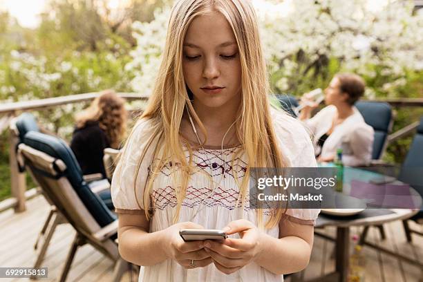 teenage girl using smart phone at yard with family sitting in background - 3 teenagers mobile outdoors stock-fotos und bilder