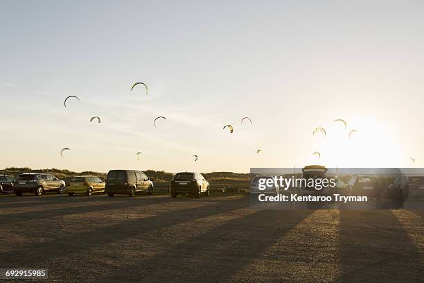 cars parked on beach against parachutes in sky during sunset - varberg stock pictures, royalty-free photos & images