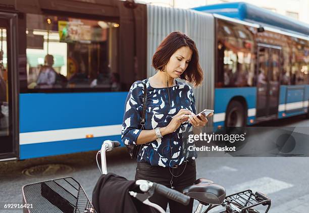 businesswoman using smart phone while standing with bicycle on city street - bike headset stock-fotos und bilder