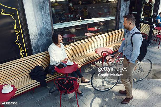 businessman with bicycle talking to female colleague sitting at sidewalk cafe - bike headset stock pictures, royalty-free photos & images