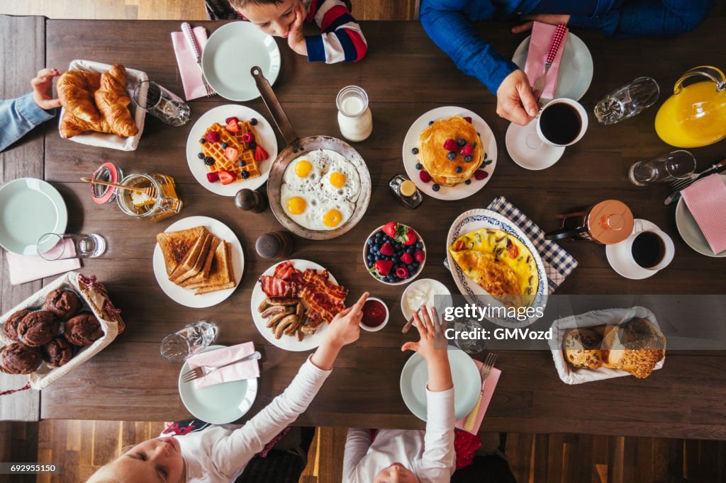 Jong gezin ontbijten met eieren, spek, yoghurt met vers fruit