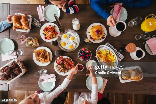 young family having breakfast with eggs, bacon, yogurt with fresh fruits - maple syrup pancakes stock pictures, royalty-free photos & images