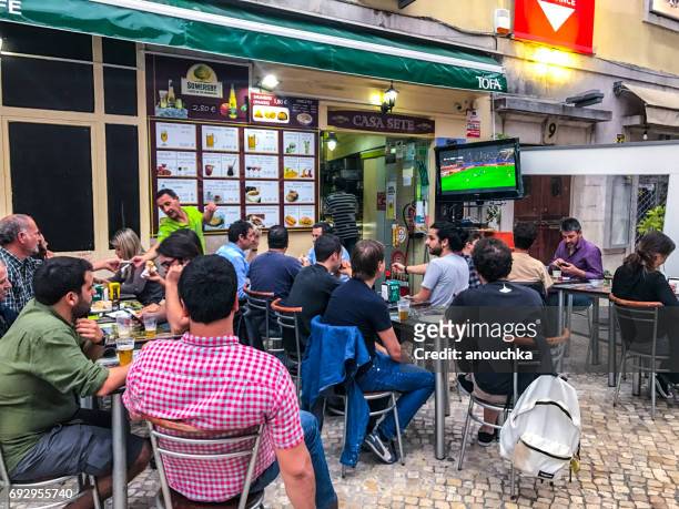 people watching football on big tv outside street cafe in lisbon. - television show stock pictures, royalty-free photos & images