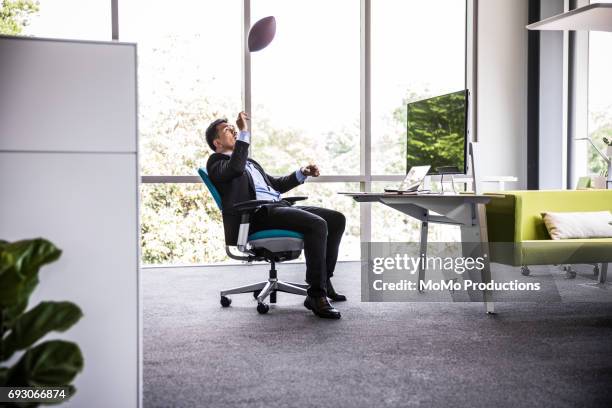 man throwing football in modern business office - lanzar actividad física fotografías e imágenes de stock